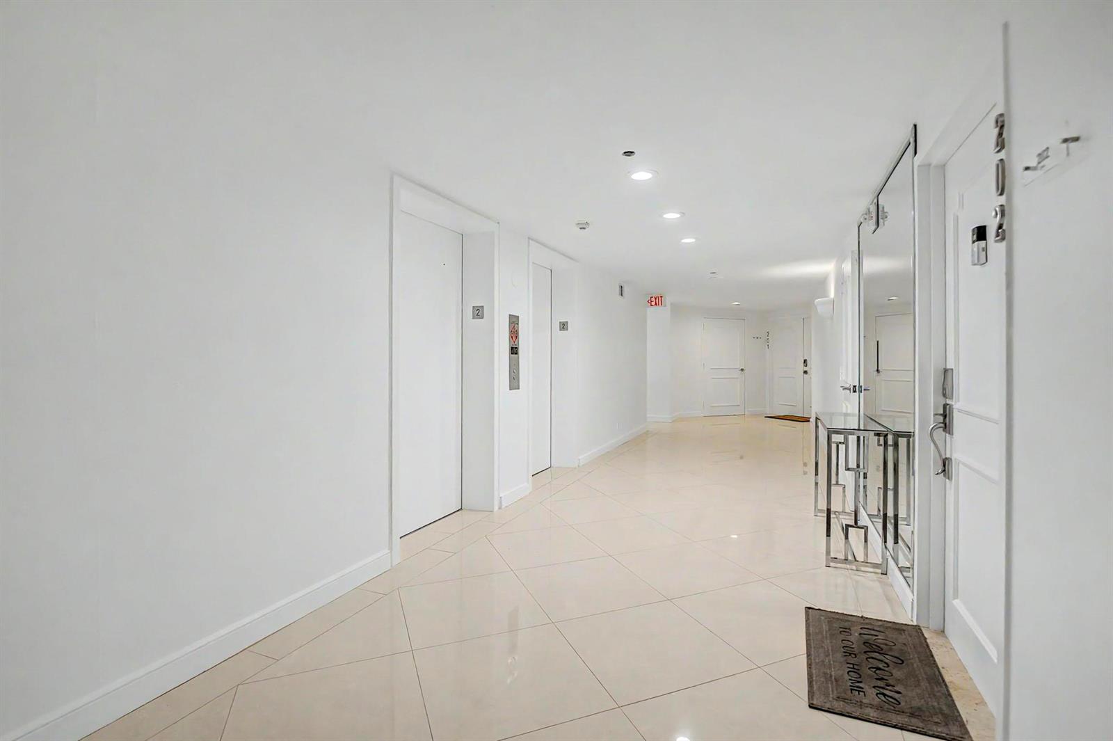A bright apartment hallway features white walls, tiled floors, two elevators, and a mirrored console — 4201 N Ocean Boulevard # 203, Boca Raton FL 33431, BOCA RATON, FL