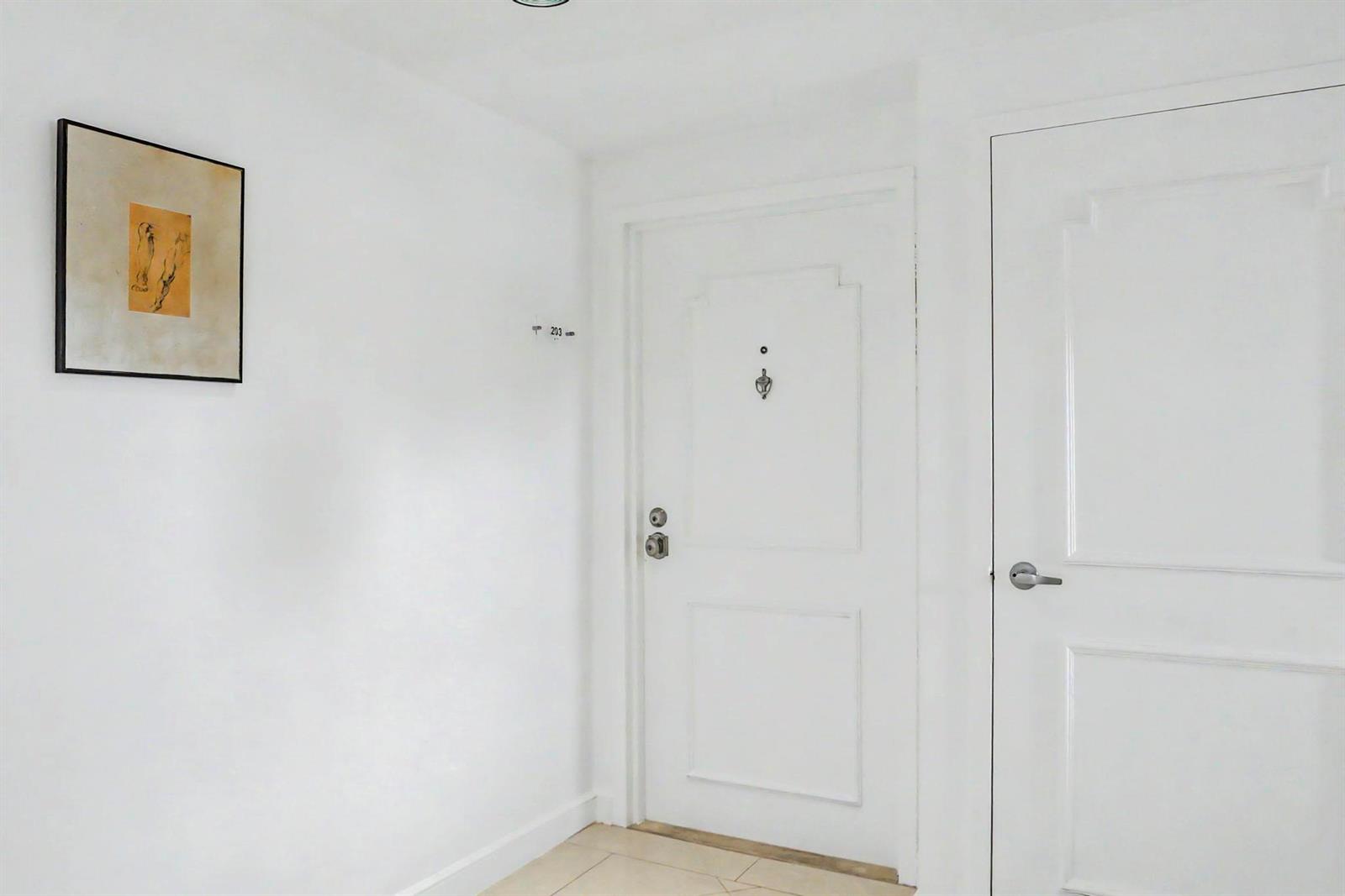 A white hallway features a framed piece of art, a door labeled 203, and tile flooring — 4201 N Ocean Boulevard # 203, Boca Raton FL 33431, BOCA RATON, FL