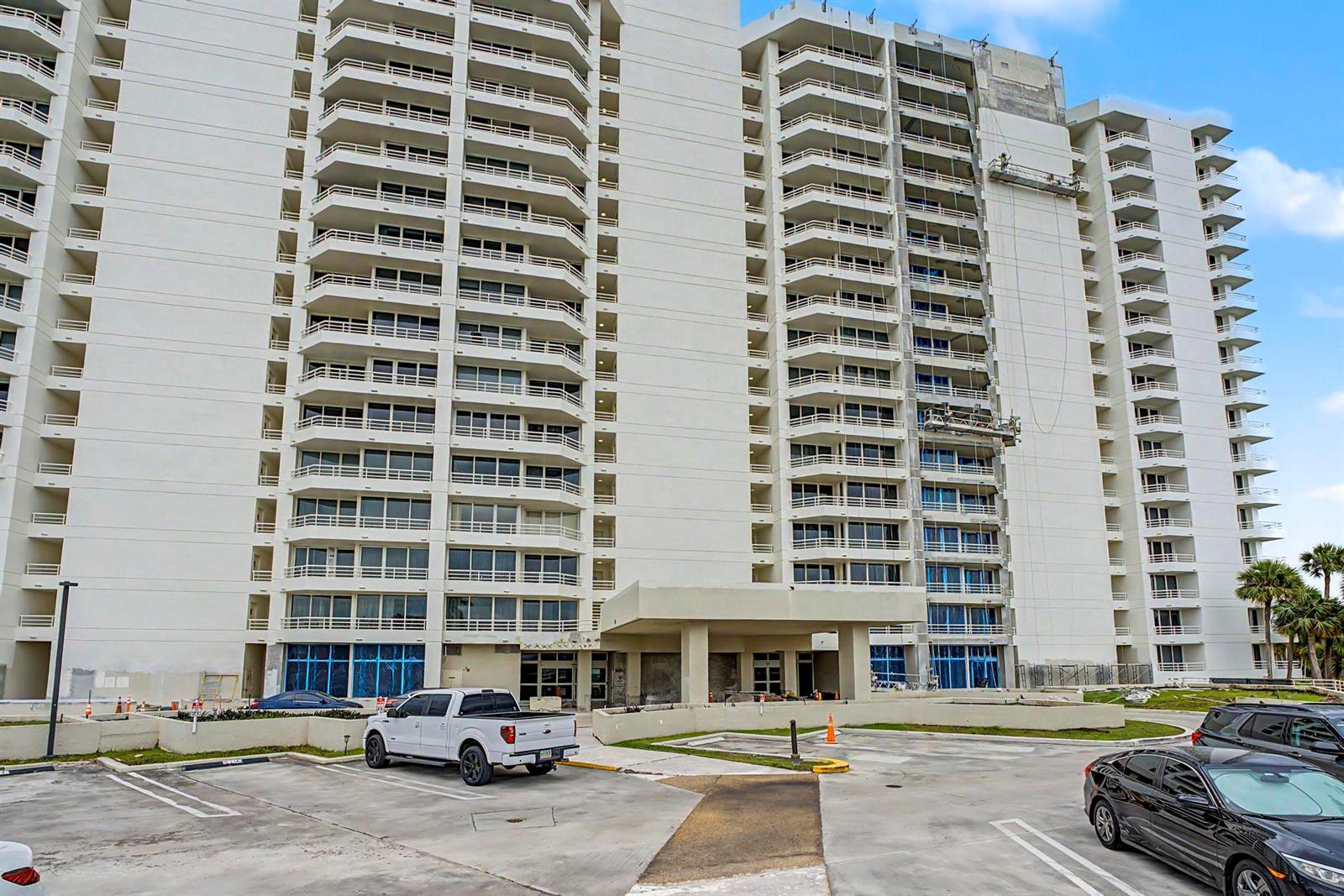 A tall white apartment building features multiple balconies and a ground-level parking lot — 4201 N Ocean Boulevard # 203, Boca Raton FL 33431, BOCA RATON, FL