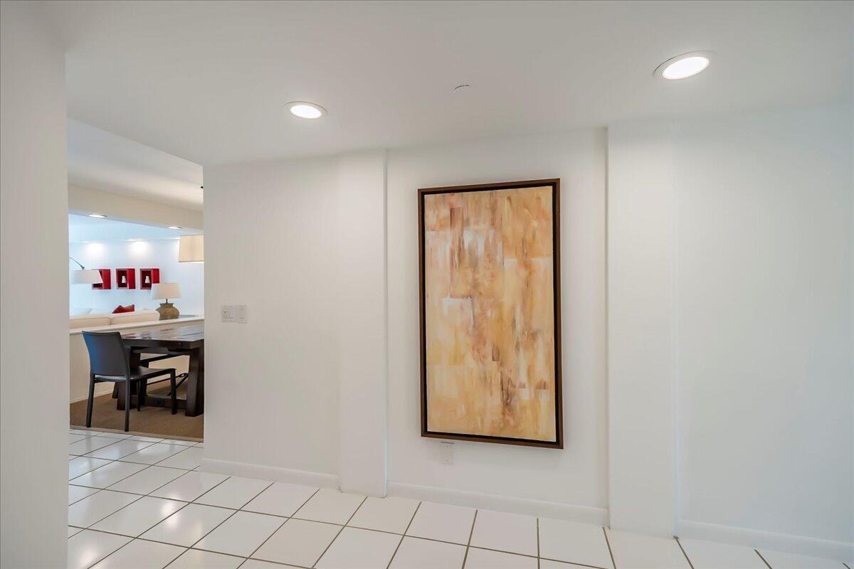 A white-tiled hallway features a large abstract painting on a wall leading to a dining area — 4201 N Ocean Boulevard # 203, Boca Raton FL 33431, BOCA RATON, FL