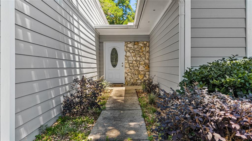 A concrete walkway leads to a white front door flanked by stone veneer siding — 11801 NW 72ND TERRACE, ALACHUA, FL
