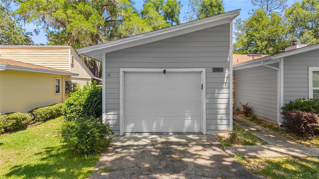 A single-car garage with gray horizontal siding and a shed roof sits between two houses — 11801 NW 72ND TERRACE, ALACHUA, FL