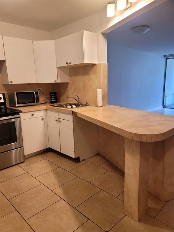 A kitchen features white cabinets, a stone countertop breakfast bar, and tan floor tiles — 1690 NE 191ST STREET UNIT 315, MIAMI, FL