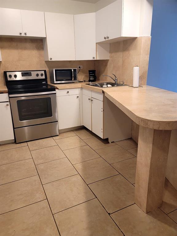 A kitchen features white cabinets, stainless steel appliances, and tan tile flooring and countertops — 1690 NE 191ST STREET UNIT 315, MIAMI, FL