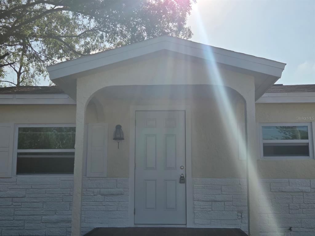 The exterior of a house features a covered entryway with a white door and stone siding — 13113 BARTOW STREET, HUDSON, FL
