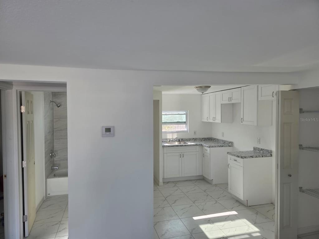 A view looking from a room into a white kitchen and an adjacent tiled bathroom — 13113 BARTOW STREET, HUDSON, FL