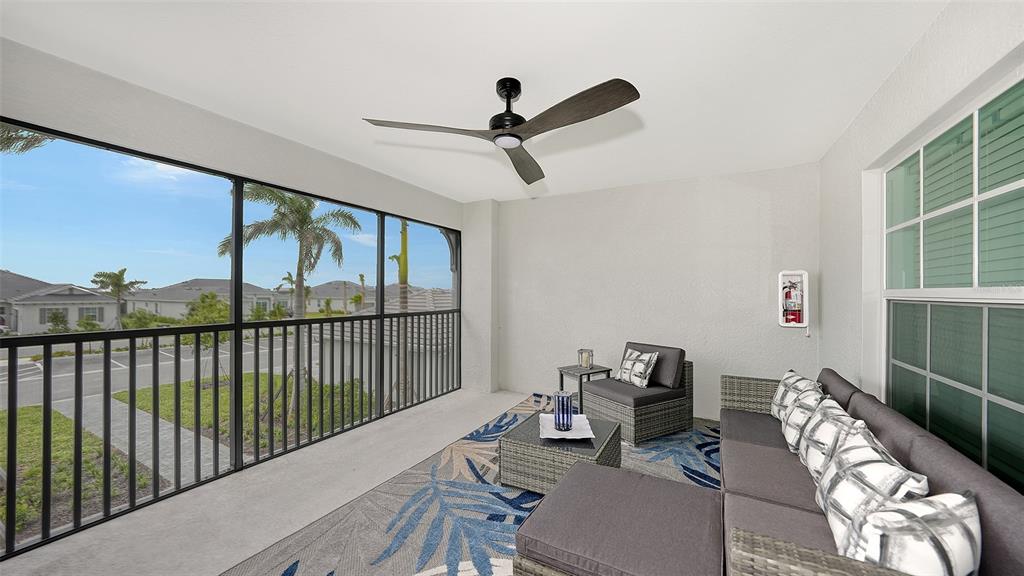 A screened-in patio features a ceiling fan, wicker furniture, and a view of the neighborhood — 12550 GALAPAGOS COURT UNIT 205, VENICE, FL