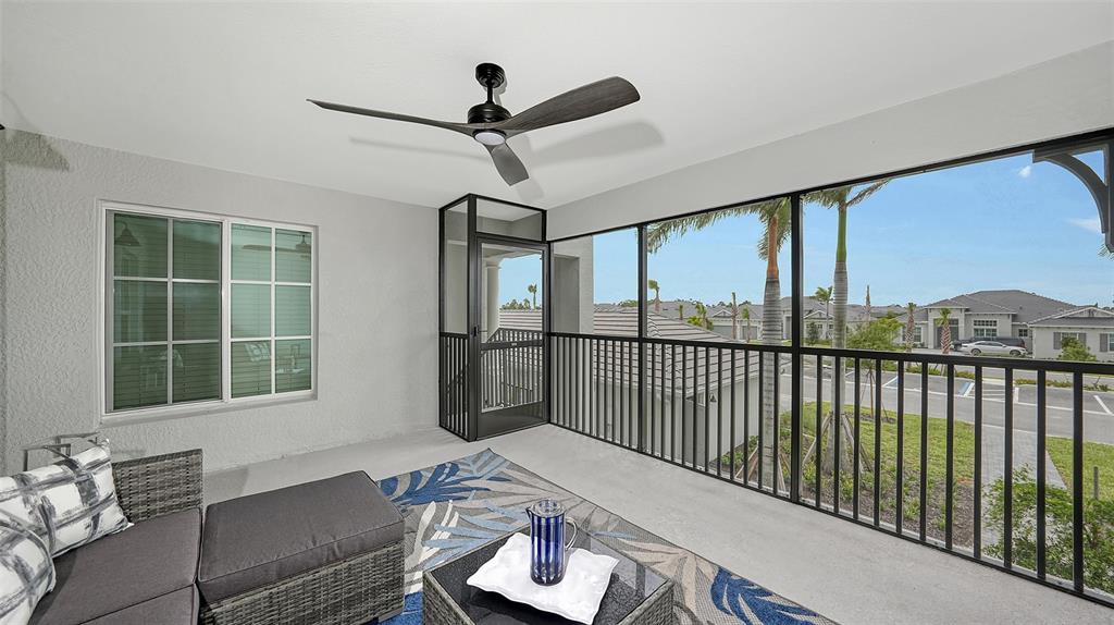 A screened-in balcony features a ceiling fan, outdoor furniture, and a view of neighborhood homes — 12550 GALAPAGOS COURT UNIT 205, VENICE, FL