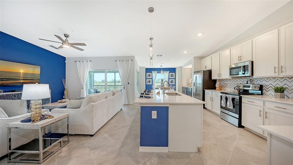 An open-concept living room and kitchen featuring white cabinetry, a blue accent wall, and tile flooring — 12550 GALAPAGOS COURT UNIT 205, VENICE, FL