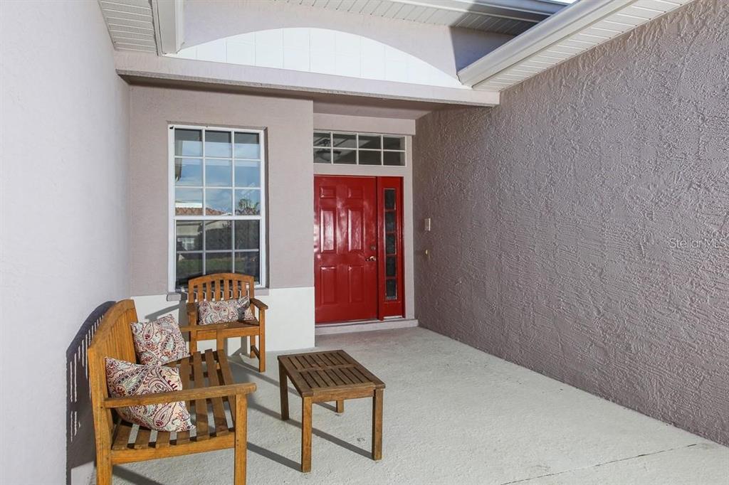 A covered front porch features a red door, a window, and wooden patio furniture — 5041 47TH STREET W, BRADENTON, FL