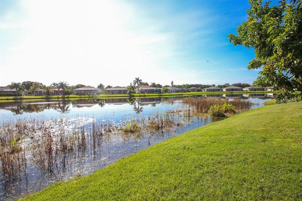 A grassy lawn overlooks a pond with houses visible in the background under a sky — 5041 47TH STREET W, BRADENTON, FL