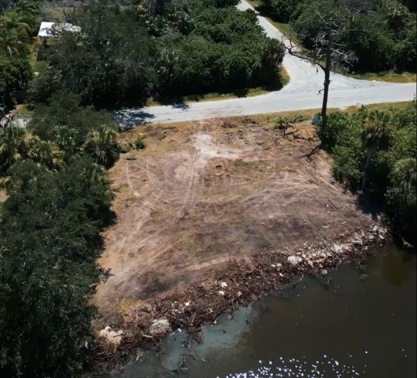 An aerial view shows a cleared, vacant waterfront lot adjacent to a paved road — 6841 OELSNER STREET, NEW PORT RICHEY, FL