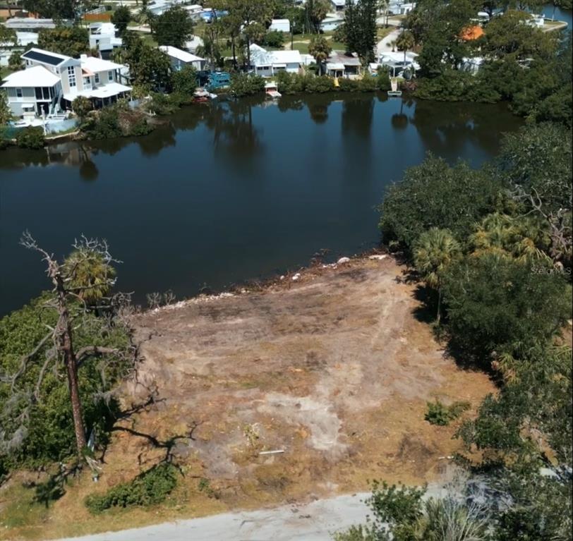 An aerial view shows a cleared, vacant waterfront lot bordered by trees and nearby houses — 6841 OELSNER STREET, NEW PORT RICHEY, FL