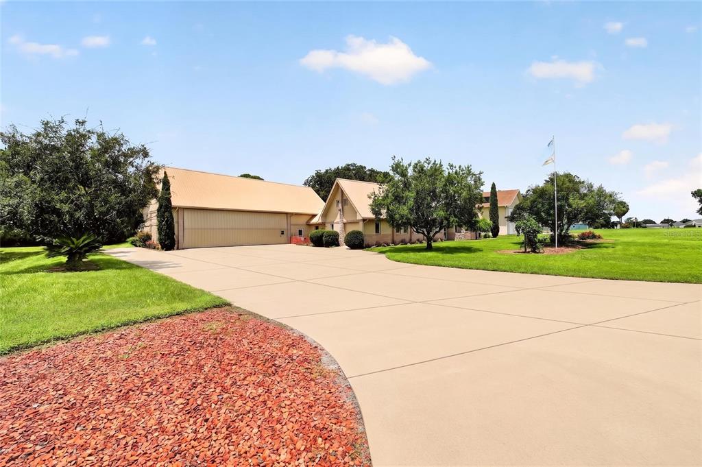 A large house with an attached hangar sits at the end of a long concrete driveway — 9726 SE 70TH TERRACE, OCALA, FL