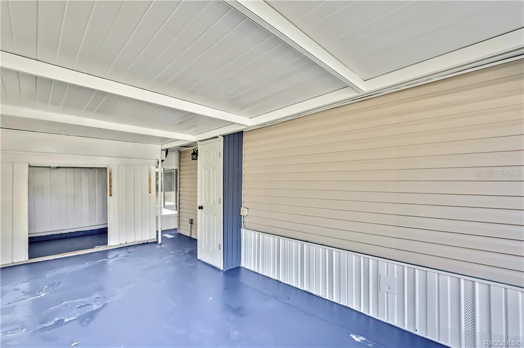 A covered patio with blue flooring, beige horizontal siding, and a white door — 8340 W AMELIA COURT, HOMOSASSA, FL