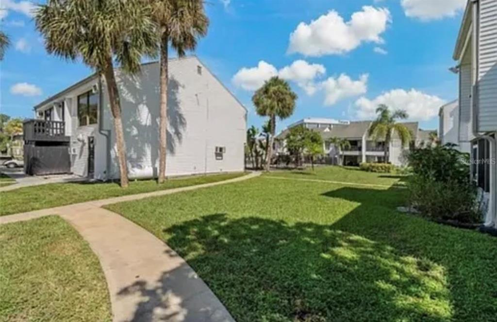 A grassy courtyard sits between two multi-story residential buildings under a bright blue sky — 654 HAVEN PLACE UNIT 654, TARPON SPRINGS, FL