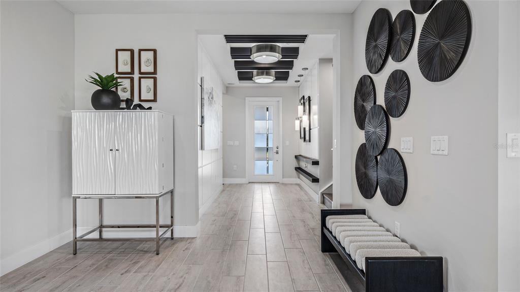 A modern entryway features wood-look tile floors, a white cabinet, and circular wall art — 1729 POINT GRACE ROAD, TAVARES, FL
