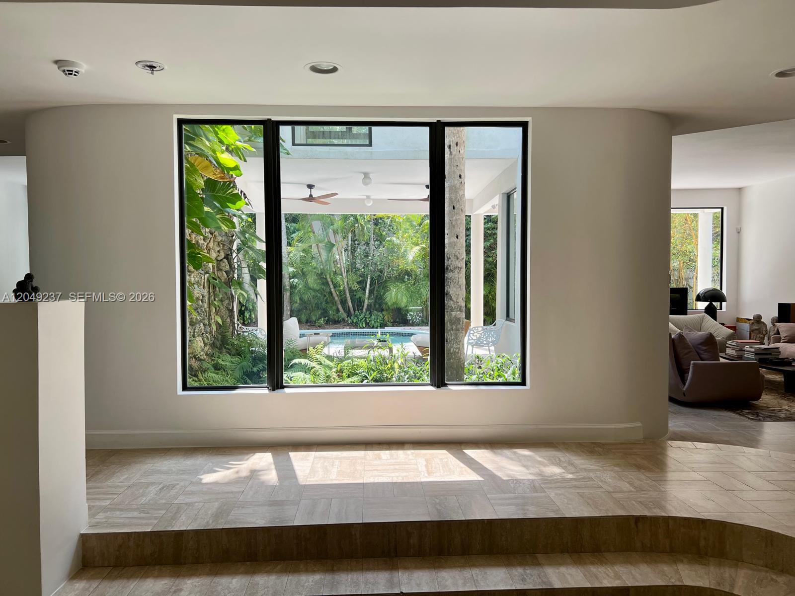 A large window overlooks a tropical patio and pool area from a tiled room — 4101 Battersea Rd # 1, Miami FL 33133, MIAMI, FL