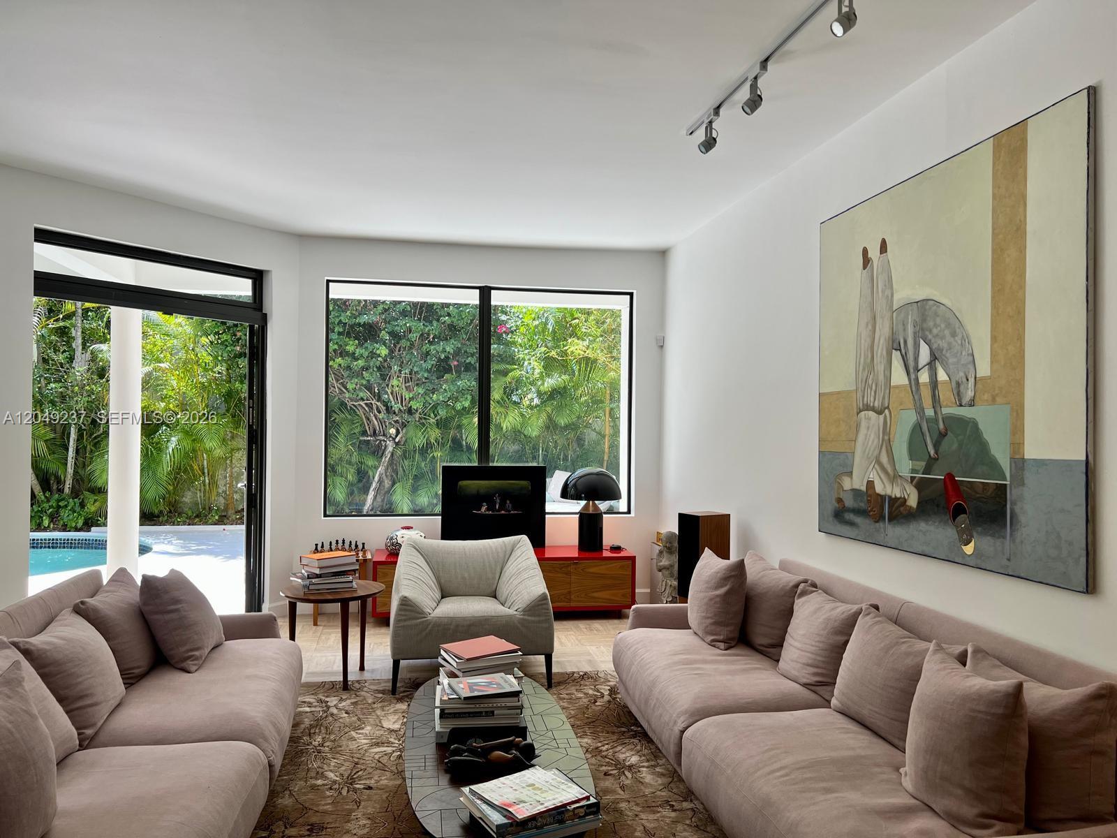 A living room features two beige sofas, a central coffee table, and large windows overlooking greenery — 4101 Battersea Rd # 1, Miami FL 33133, MIAMI, FL