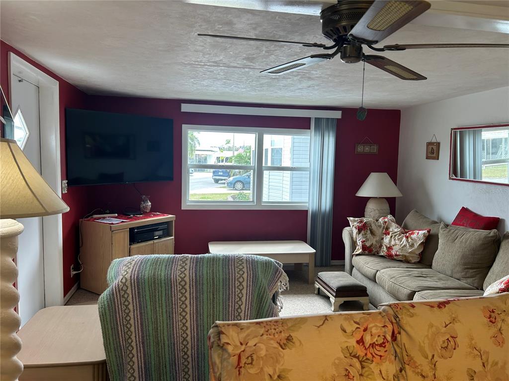 A living room features red walls, a ceiling fan, a television, and beige furniture — 5025 BRAE BURN AVENUE, SARASOTA, FL
