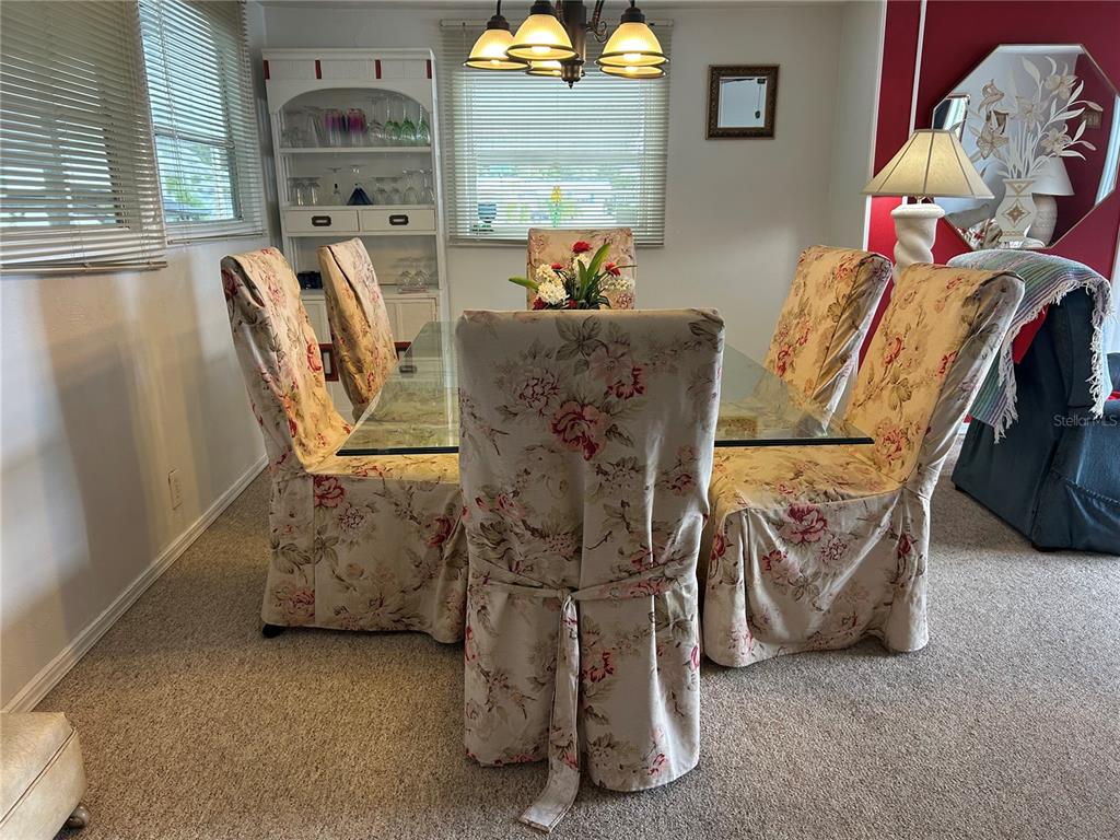 A dining room features a glass-topped table with six floral-patterned slipcovered chairs on carpet — 5025 BRAE BURN AVENUE, SARASOTA, FL