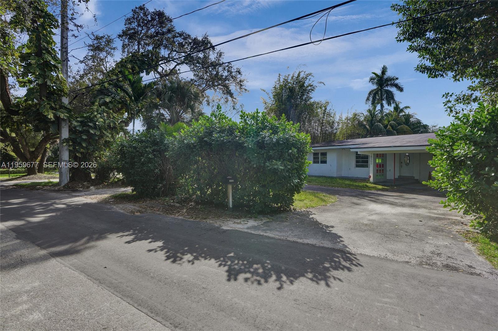 A white single-story house sits behind a large hedge next to a paved driveway — 18500 NE 23rd Ct, Miami FL 33180, MIAMI, FL