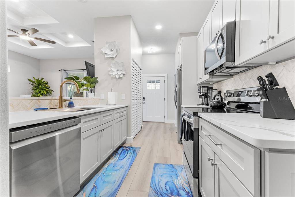 A modern kitchen features light gray cabinets, white countertops, stainless steel appliances, and blue rugs — 2047 ROSELAWN STREET, SARASOTA, FL