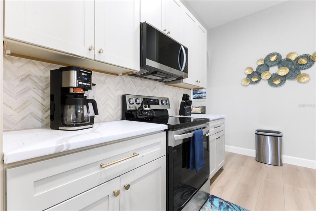 A modern kitchen features white cabinets, marble-look countertops, stainless steel appliances, and a herringbone backsplash — 2047 ROSELAWN STREET, SARASOTA, FL