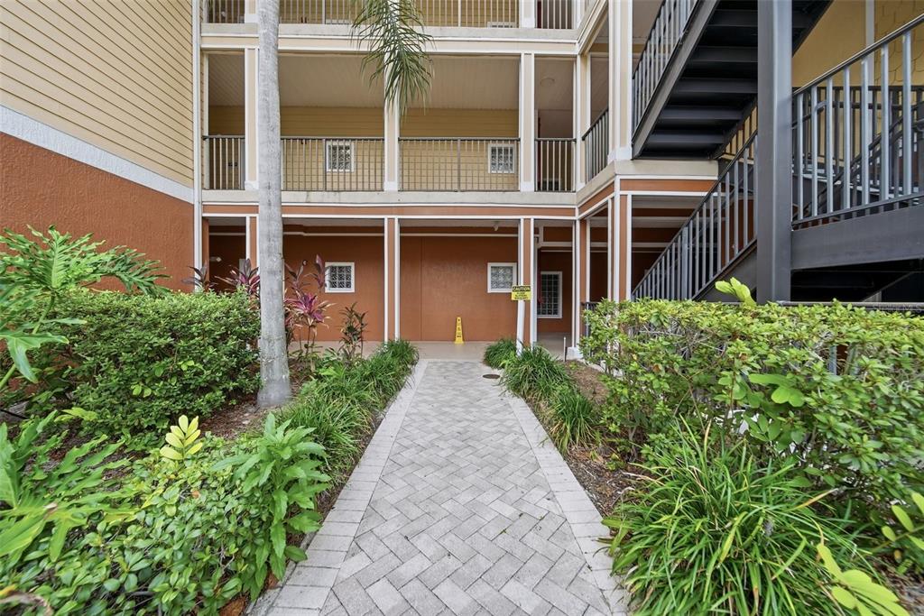A paved walkway leads to the ground floor entrance of a multi-story apartment building — 9051 TREASURE TROVE LANE UNIT 104, KISSIMMEE, FL