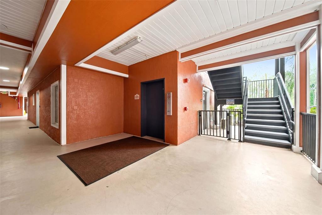 An outdoor corridor features an elevator, a staircase with a metal railing, and concrete flooring — 9051 TREASURE TROVE LANE UNIT 104, KISSIMMEE, FL