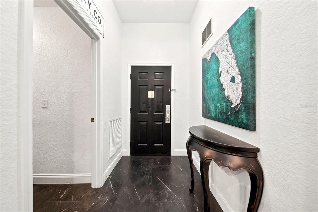 An entryway features a black door, dark marble-look tile flooring, and a Florida wall art piece — 9051 TREASURE TROVE LANE UNIT 104, KISSIMMEE, FL