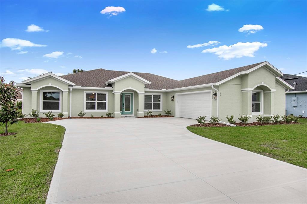 A single-story house with light green stucco siding, a concrete driveway, and a two-car garage — 18 CENTRAL PLACE, PALM COAST, FL