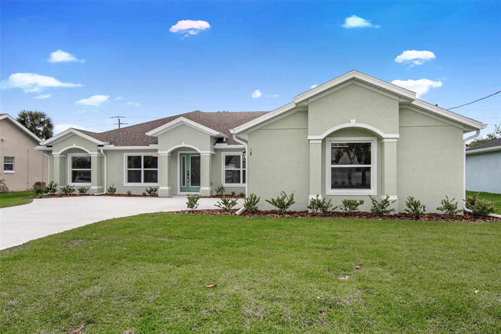 A single-story house with light green stucco siding, a teal front door, and a concrete driveway — 18 CENTRAL PLACE, PALM COAST, FL