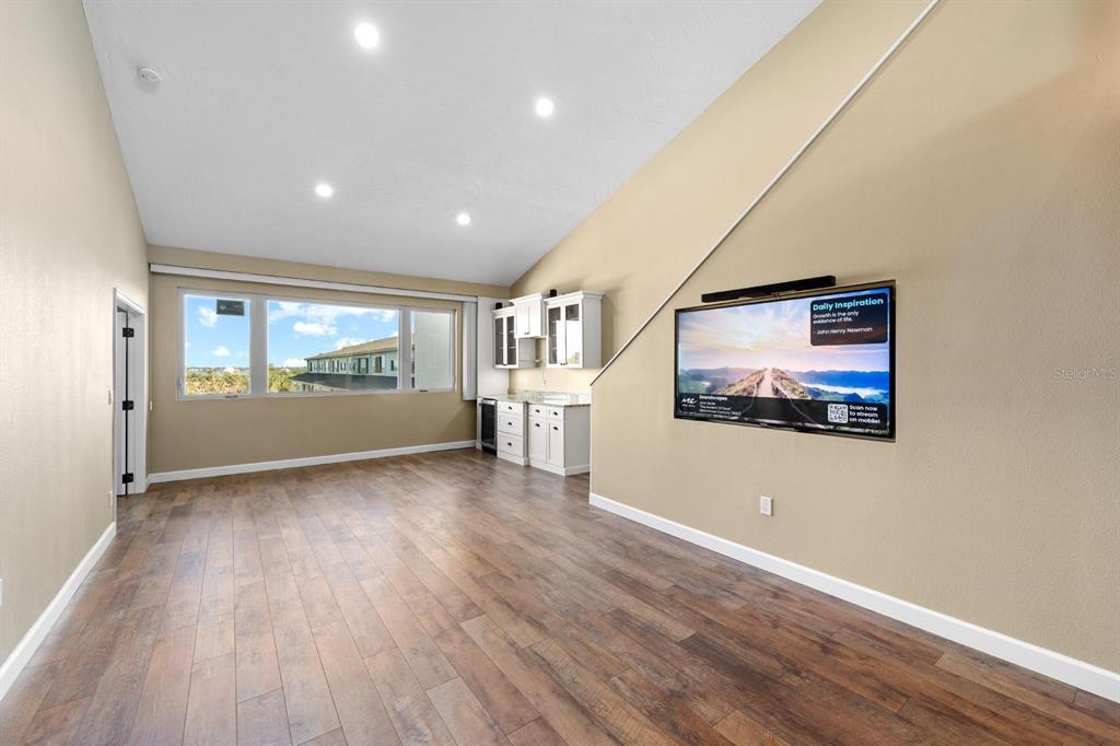 A room with wood-look flooring, a vaulted ceiling, a wet bar, and a wall-mounted television — 9604 CORTEZ ROAD W UNIT 136, BRADENTON, FL