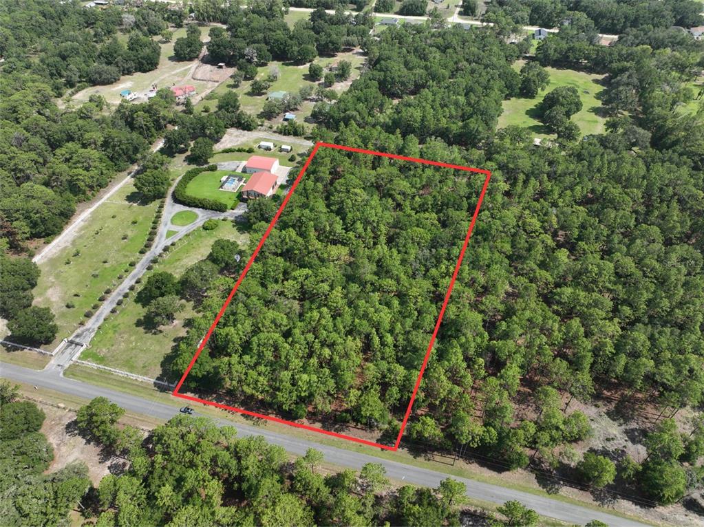 An aerial view shows a rectangular, wooded lot outlined in red next to a house — SW 97TH PL, DUNNELLON, FL