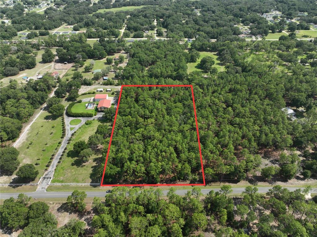 An aerial view shows a rectangular, wooded plot of land outlined in red near a road — SW 97TH PL, DUNNELLON, FL