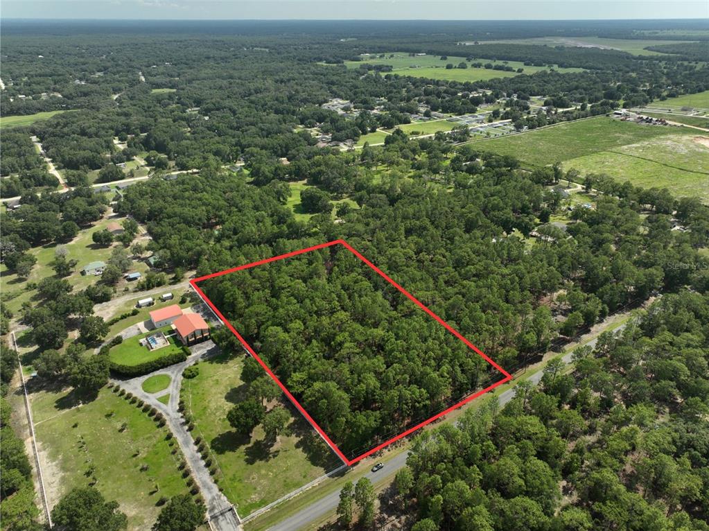 An aerial view shows a rectangular wooded lot outlined in red next to a house — SW 97TH PL, DUNNELLON, FL