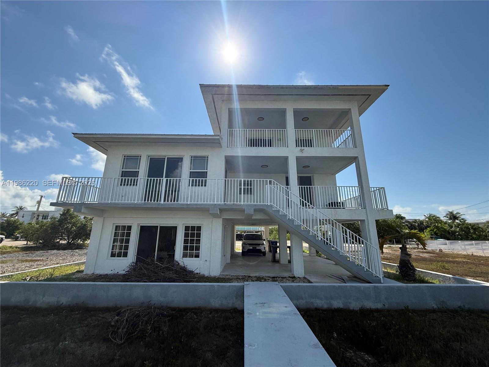 A three-story white house with an elevated living area and an outdoor staircase — 27403 Antigua Ln, Lower Keys FL 33042, LOWER KEYS, FL