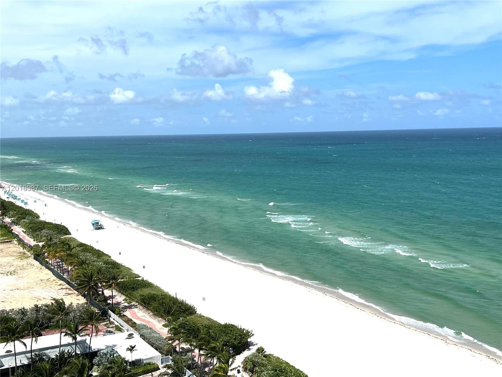 An aerial view shows a white sand beach meeting the turquoise ocean under a cloudy sky — 6515 Collins Ave # 1801, Miami Beach FL 33141, MIAMI BEACH, FL