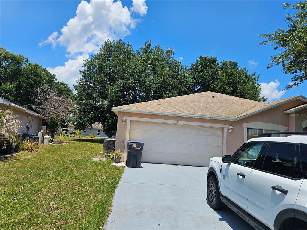 A single-story house with a beige exterior, a two-car garage, and a concrete driveway — 7 HADDOCK WAY, KISSIMMEE, FL