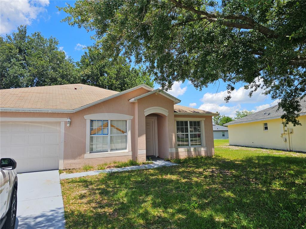 A single-story peach-colored house with a garage and a front yard under a tree — 7 HADDOCK WAY, KISSIMMEE, FL