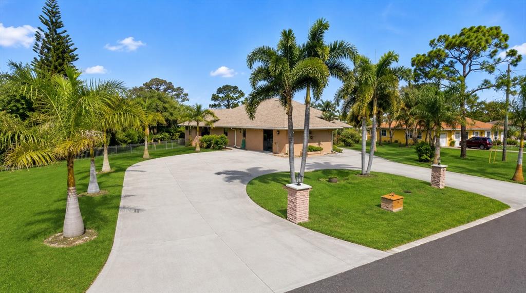 A tan house with a large circular concrete driveway and palm trees in the front yard — 1710 PARKER DRIVE, ENGLEWOOD, FL