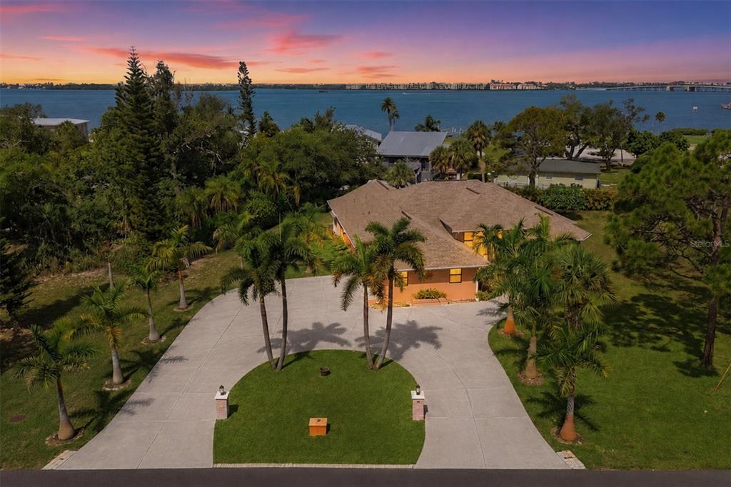 An aerial view shows a house with a circular driveway and palm trees near water — 1710 PARKER DRIVE, ENGLEWOOD, FL