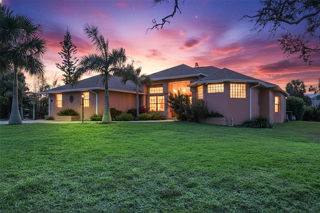 A single-story house with a tan exterior and palm trees sits on a grassy lawn — 1710 PARKER DRIVE, ENGLEWOOD, FL