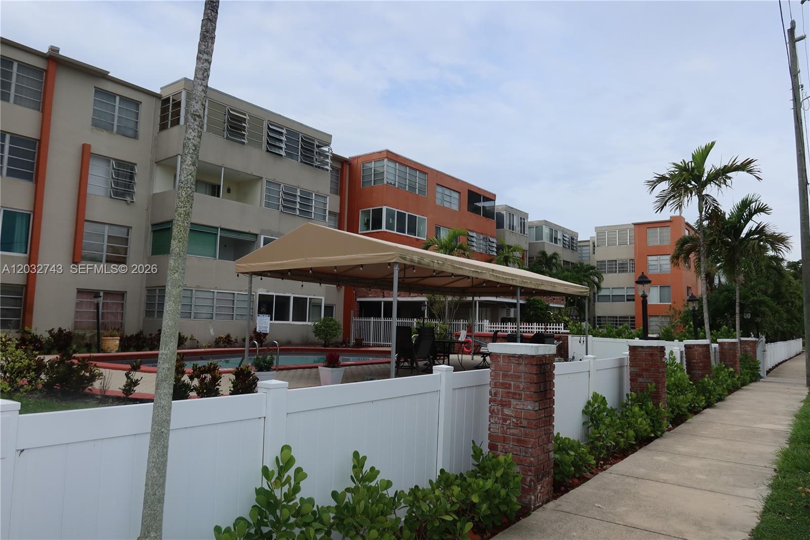 An outdoor swimming pool area is enclosed by a white fence next to apartment buildings — 1850 NE 169th St # 312, North Miami Beach FL 33162, NORTH MIAMI BEACH, FL