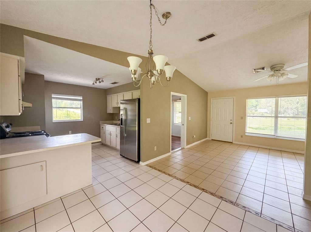 A kitchen with white cabinets and tile flooring opens into a dining area with windows — 1870 SW VALENCIA HEIGHTS AVENUE, DUNNELLON, FL