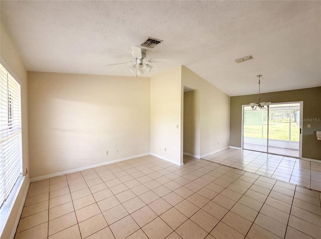 An open-concept living and dining area features beige tile flooring and a vaulted ceiling — 1870 SW VALENCIA HEIGHTS AVENUE, DUNNELLON, FL
