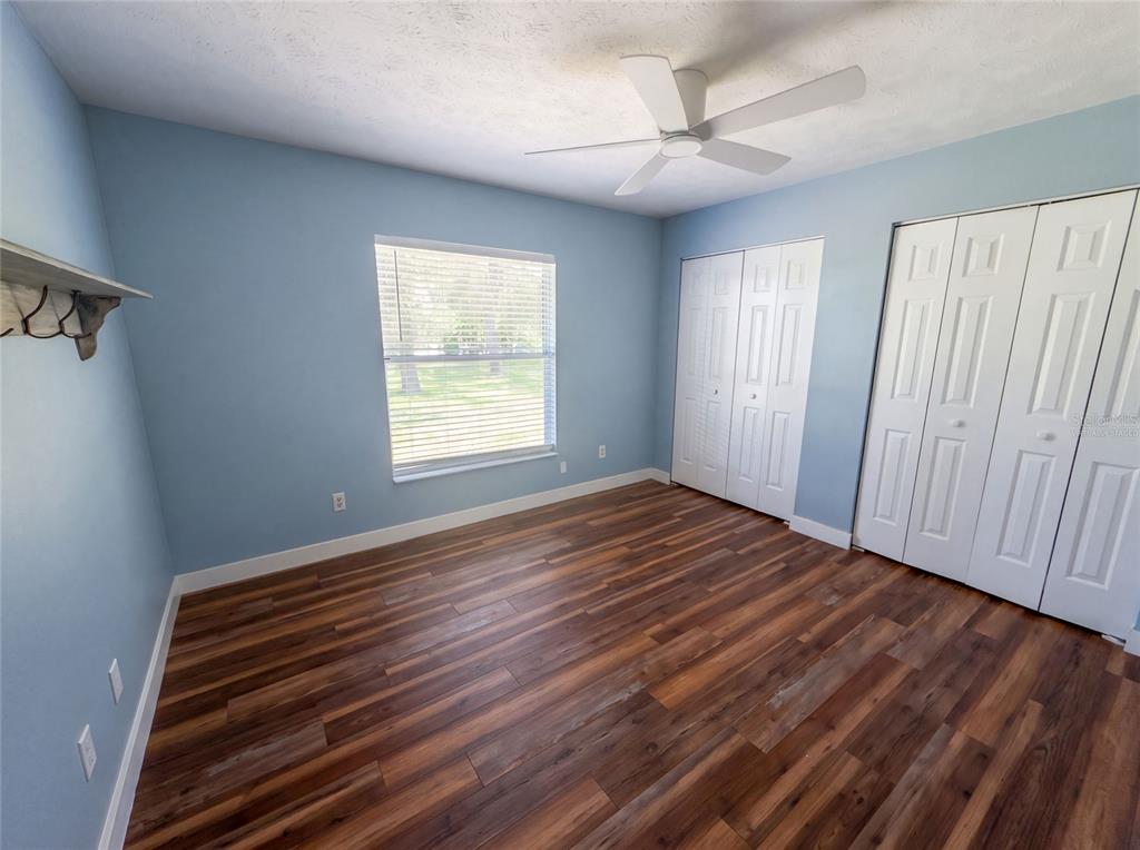 A bedroom with light blue walls, wood-look flooring, a ceiling fan, and white closet doors — 1870 SW VALENCIA HEIGHTS AVENUE, DUNNELLON, FL