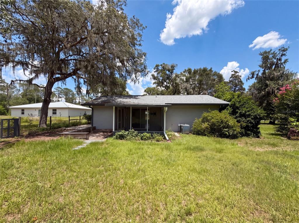 The exterior of a gray house features a screened-in porch, a wooden deck, and large trees — 1870 SW VALENCIA HEIGHTS AVENUE, DUNNELLON, FL