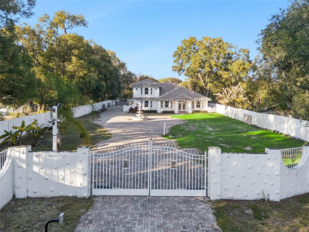 A gated driveway leads to a two-story house with a fountain and surrounding white fence — 20 REWIS STREET, OCOEE, FL